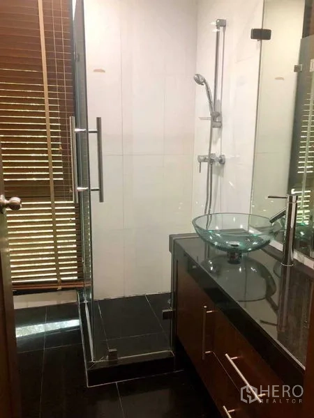 Townhouse for rent in Khlong Toei, Bangkok - Bathroom with a glass‑enclosed shower, vessel sink on a dark countertop, and wooden blinds.
