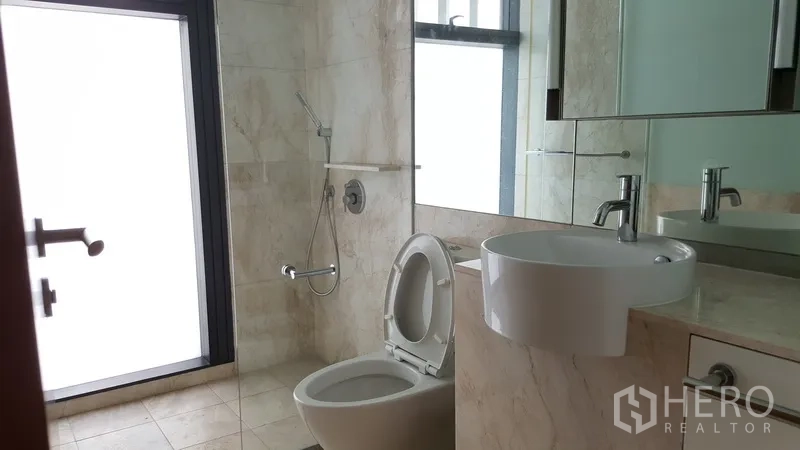 Condominium for rent in Sathon, Bangkok - Guest bathroom with walk-in shower, toilet, large mirror, and marble tiles.