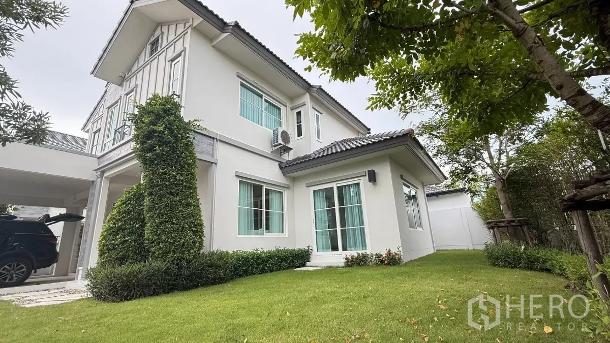 บ้าน ให้เช่าในBang Phli, Samut Prakan - มุมด้านข้างของบ้านสีขาวสองชั้นพร้อมหน้าต่างบานใหญ่และสนามหญ้าเรียบสวย.