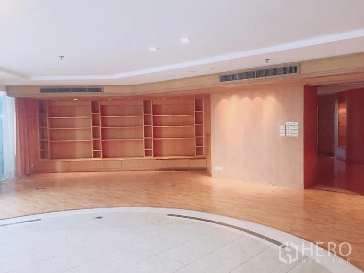 Condominium for rent in Watthana, Bangkok - Spacious lounge with a curved recessed tile area and full-height wooden bookshelves.
