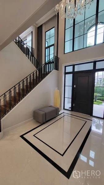 Detached House for rent or sale in Saphan Sung, Bangkok - Double-height foyer with chandelier, black-framed windows and staircase in a luxury house.