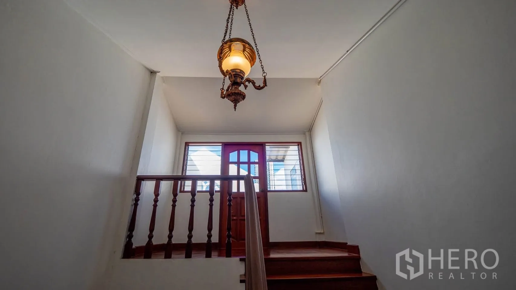 Townhouse for rent in Watthana, Bangkok - Stair landing with a vintage hanging chandelier and light-filled glass door.