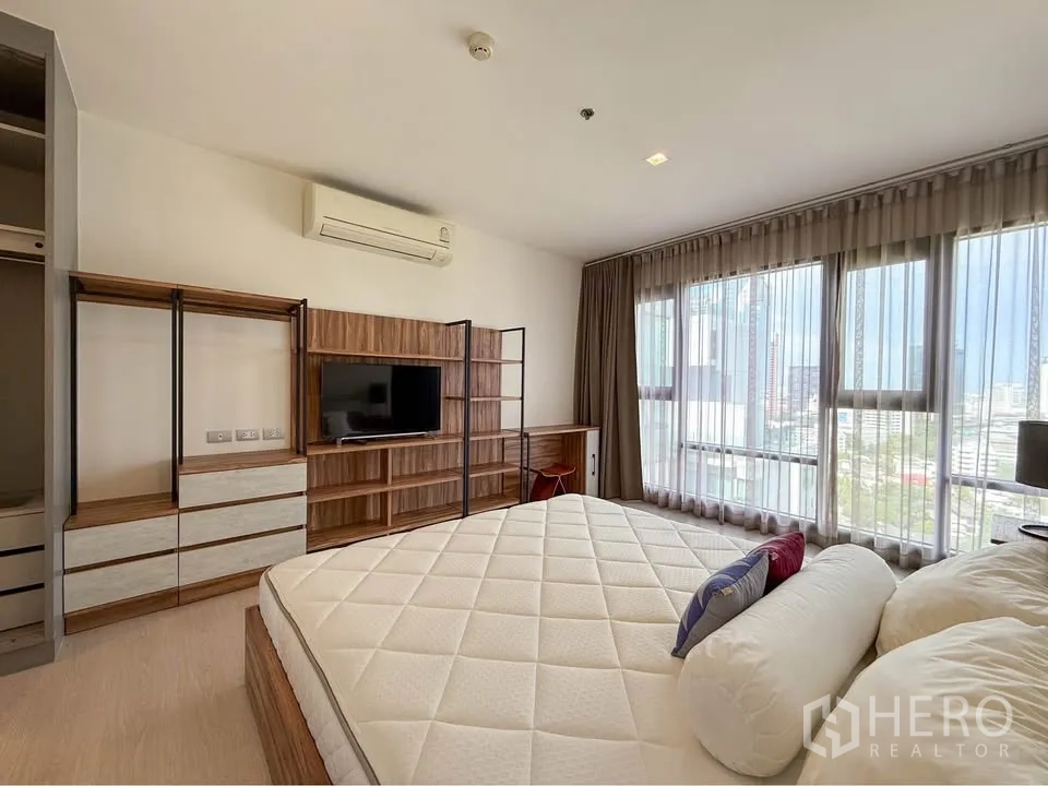Condominium for rent in Khlong Toei, Bangkok - Large room with wall-to-wall windows, custom shelving and TV opposite the bed.