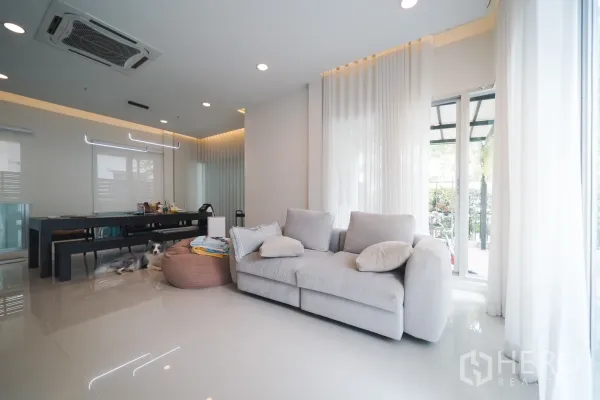 บ้าน ให้เช่าหรือขายในSaphan Sung, Bangkok - ห้องนั่งเล่นสว่างด้วยหน้าต่างบานใหญ่ ผ้าม่านโปร่ง และโซฟาสีเทา เชื่อมต่อสู่เฉลียง