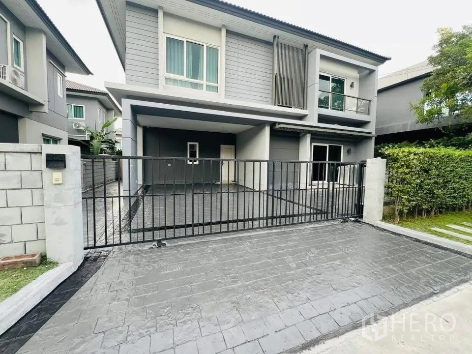 บ้านเดี่ยว for rent in Prawet, Bangkok - ด้านหน้าบ้านสองชั้นสไตล์โมเดิร์น มีกำแพงรั้ว ประตูเลื่อน ที่จอดรถในร่ม และสนามหญ้าเล็ก.