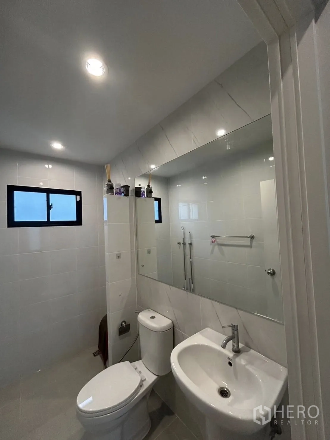 Detached House for rent in Khlong Sam Wa, Bangkok - Contemporary bathroom with wide mirror, basin, toilet and windowed shower area.