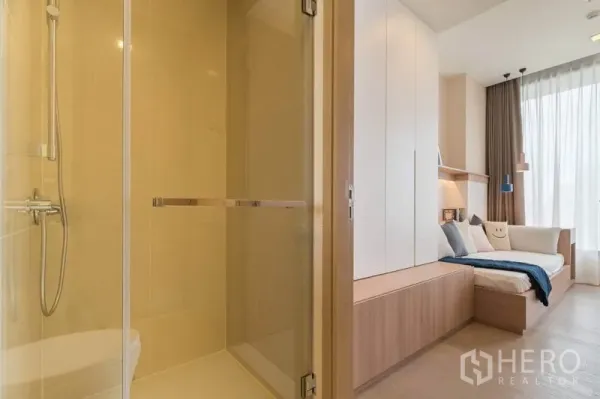 Condominium for rent in Watthana, Bangkok - Glass-enclosed shower beside a cozy bedroom with built-in wardrobes and a daybed under tall curtains.