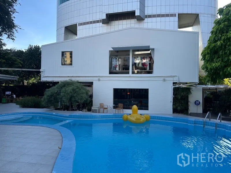 Retail Space for rent in Khlong Toei, Bangkok - Exterior of a low-rise white building with large windows overlooking a blue swimming pool and patio chairs.