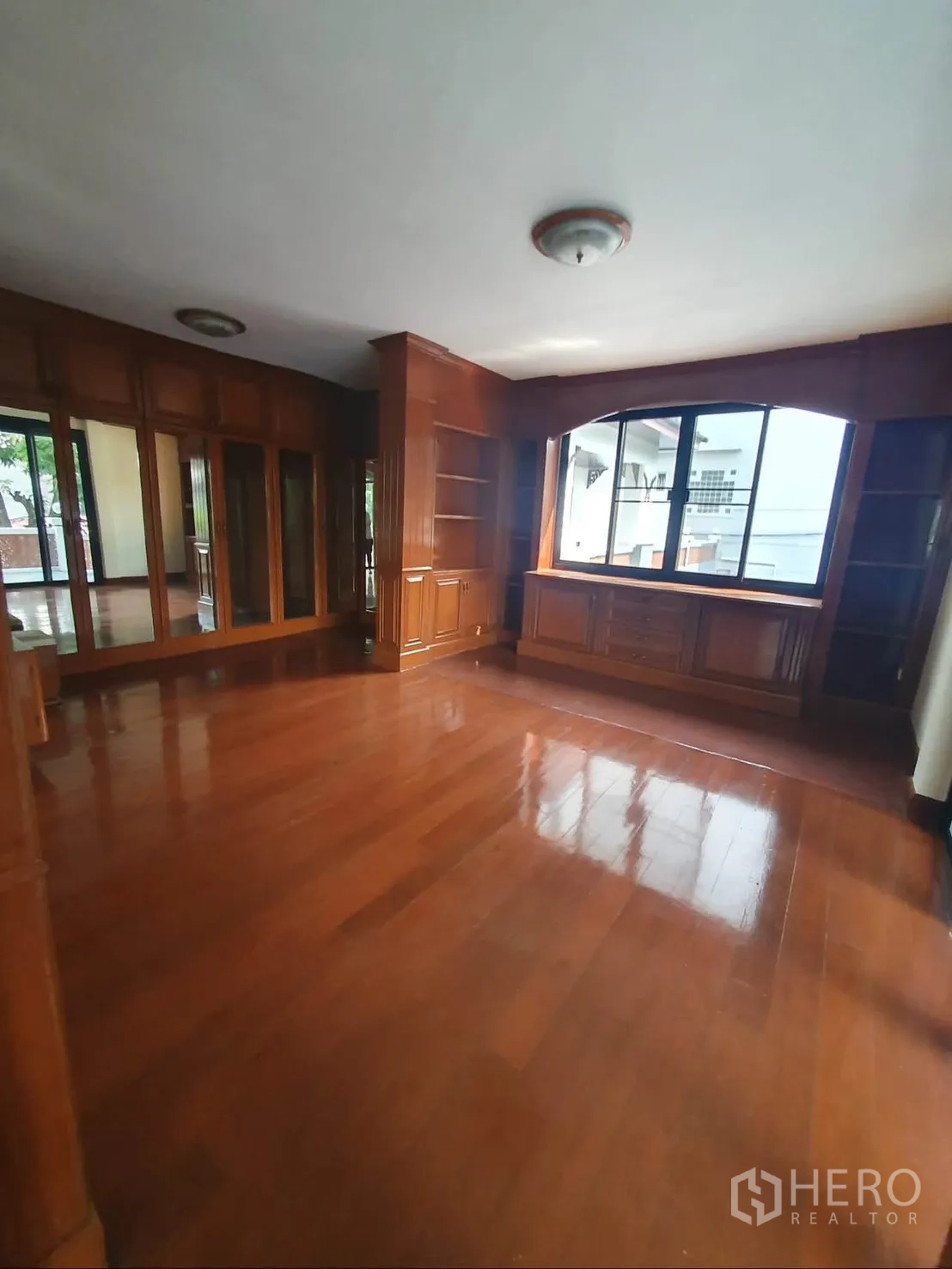 Detached House for rent in Sathon, Bangkok - Room with polished wooden floor, large window, and built-in shelves and cabinets.