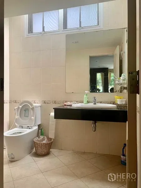 独立式住宅 出租在Prawet, Bangkok - 明亮瓷砖浴室，带窗户、大镜子与悬空洗手台。