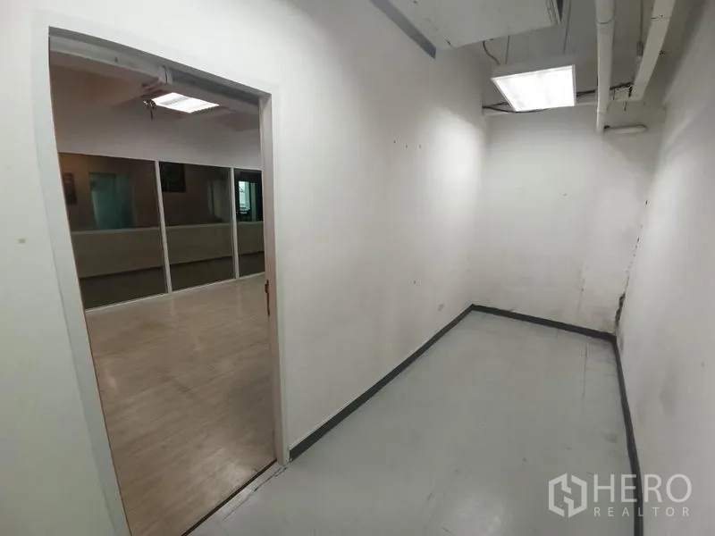 สำนักงาน ให้เช่าในRatchathewi, Bangkok - พื้นที่โถงแคบสีขาวเชื่อมไปยังออฟฟิศกั้นกระจก พร้อมไฟฟลูออเรสเซนต์บนเพดาน.