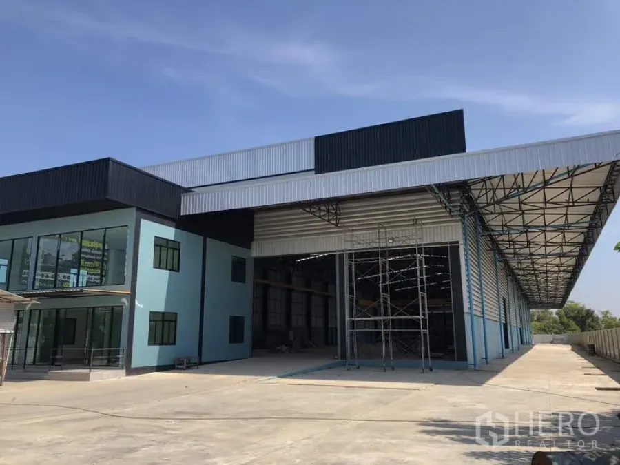Factory for rent in Lam Luk Ka, Pathum Thani - Covered loading bay and large warehouse facade with a high steel roof and spacious driveway.