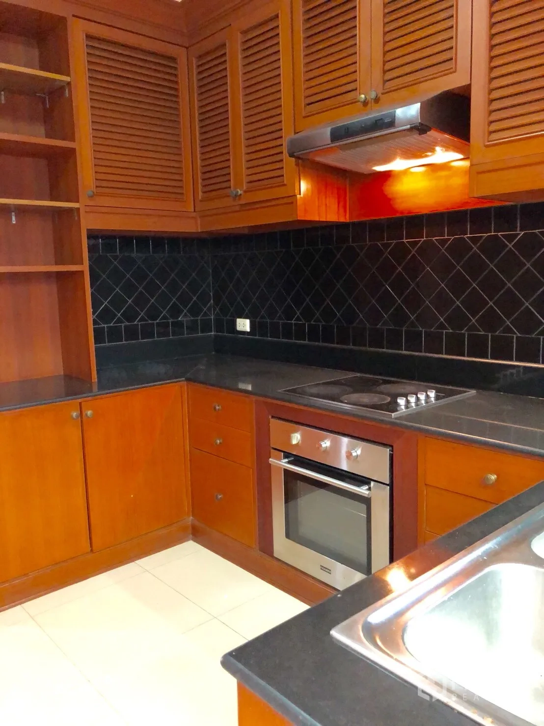 Townhouse for rent in Khlong Toei, Bangkok - Separate kitchen with wooden cabinets, black countertops, oven and cooktop.