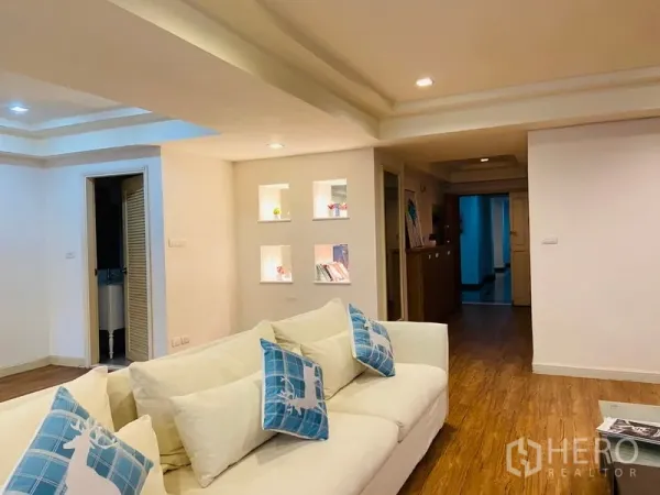 Condominium for rent in Watthana, Bangkok - Cozy lounge with a white sofa and illuminated display niches along the hallway on warm wood flooring.