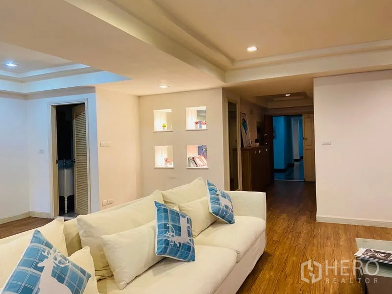 Condominium for rent in Watthana, Bangkok - Cozy lounge with a white sofa and illuminated display niches along the hallway on warm wood flooring.