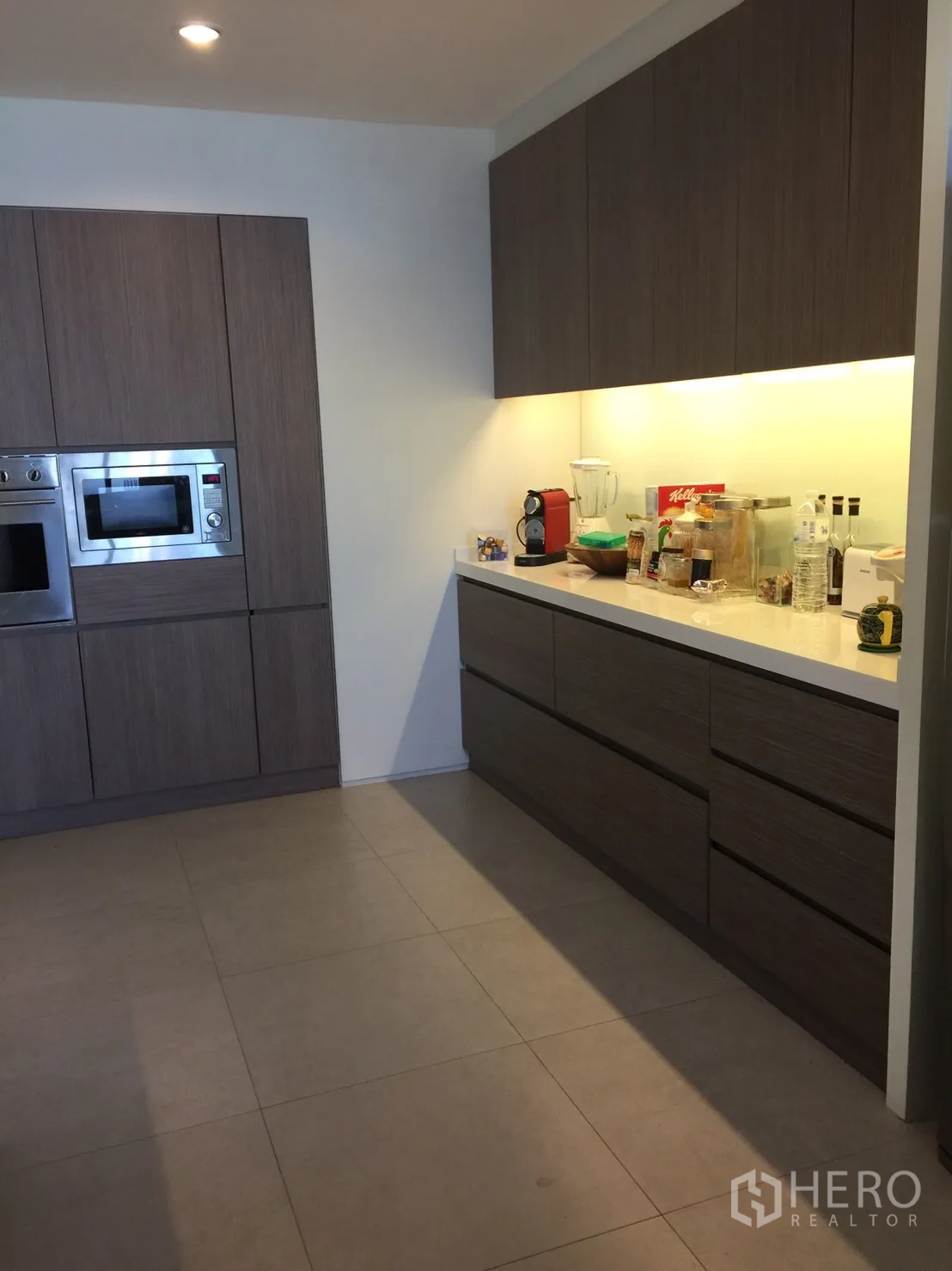 Condominium for rent in Watthana, Bangkok - Kitchen view showing built-in oven and microwave, long countertop and under-cabinet lighting.