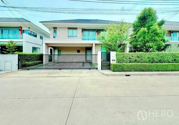 บ้าน ขายในLat Krabang, Bangkok - ด้านหน้าบ้านสองชั้นพร้อมรั้วเหล็กสีดำและพื้นที่สวน