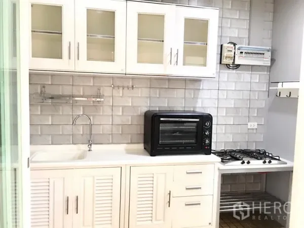 ทาวน์เฮาส์ ให้เช่าในPrawet, Bangkok - ครัวบิวต์อินสีขาวพร้อมอ่างล้างจาน เตาแก๊ส เตาอบ และผนังกระเบื้องลายอิฐ.