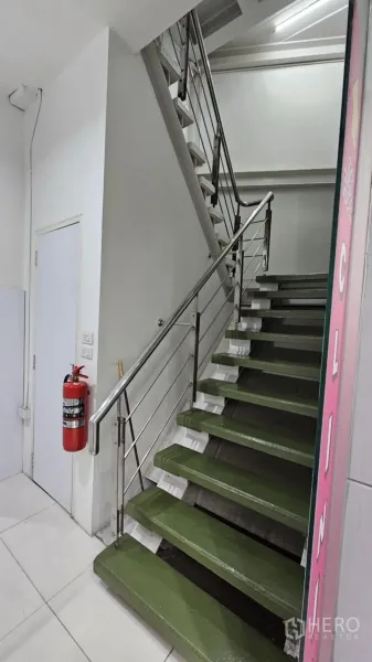 零售空间 出租在Watthana, Bangkok - 室内楼梯，绿色踏步与不锈钢扶手，墙上有灭火器。