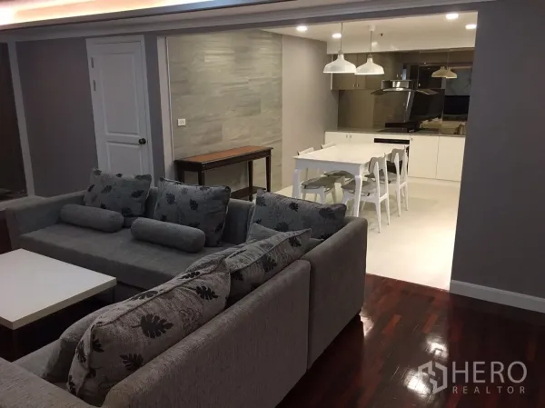 Condominium for rent in Watthana, Bangkok - Cozy living area with grey sectional sofas and coffee table opening to a bright kitchen and dining zone.