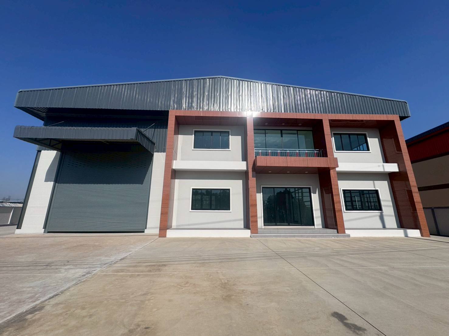 工厂 出售在Mueang Samut Sakhon, Samut Sakhon - 现代化工厂外立面，设大型卷闸门、两层办公区与宽阔混凝土地面。