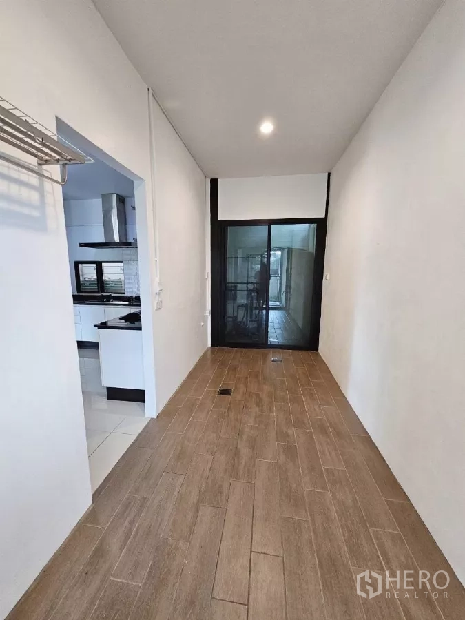 Detached House for rent or sale in Don Mueang, Bangkok - Utility corridor with wood-look tiles and sliding glass door to laundry area.