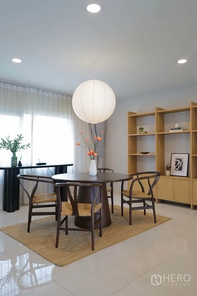 บ้านเดี่ยว for rent or sale in Bang Phli, Samut Prakan - มุมรับประทานอาหารสว่างด้วยโต๊ะไม้ทรงกลม เก้าอี้หวาย และโคมทรงกลมริมหน้าต่างบานใหญ่