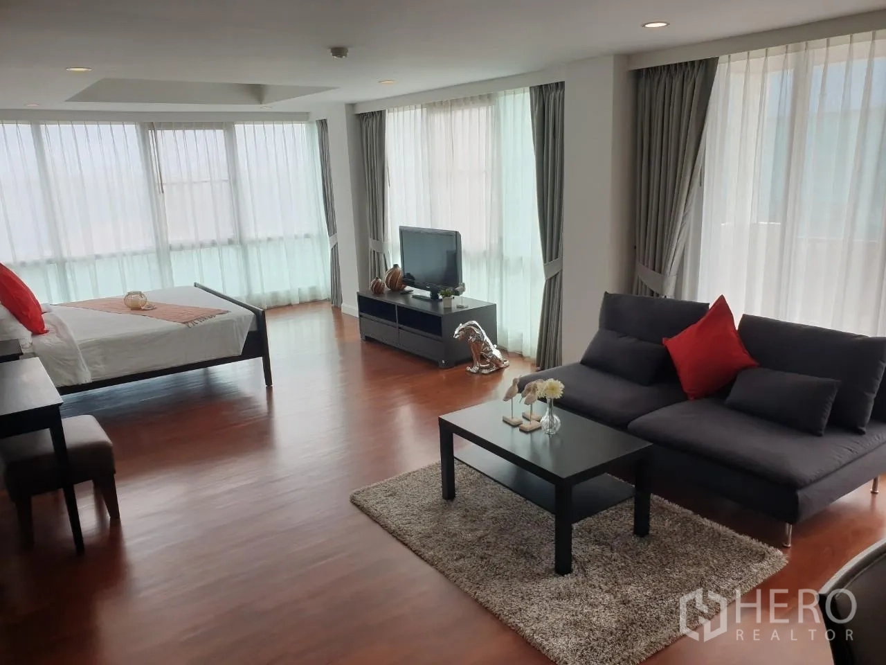 Apartment for rent in Bang Rak, Bangkok - Corner suite showing bed, sofa seating and wraparound windows.