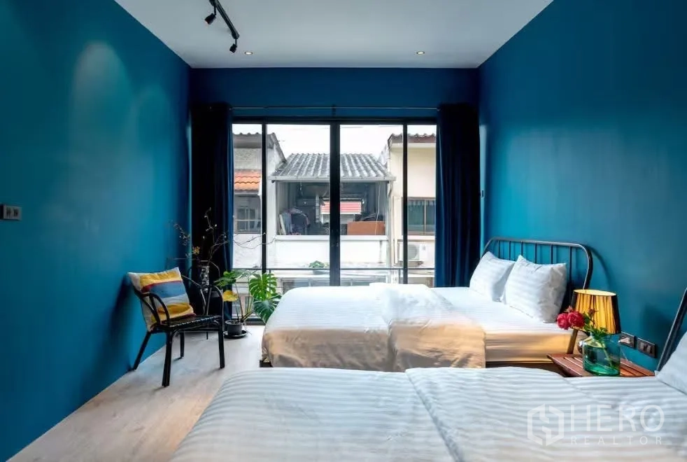 ทาวน์เฮาส์ for rent in Watthana, Bangkok - ห้องนอนสว่างไสว มีเตียงคู่ ผนังสีน้ำเงิน และหน้าต่างบานใหญ่เปิดสู่ระเบียง