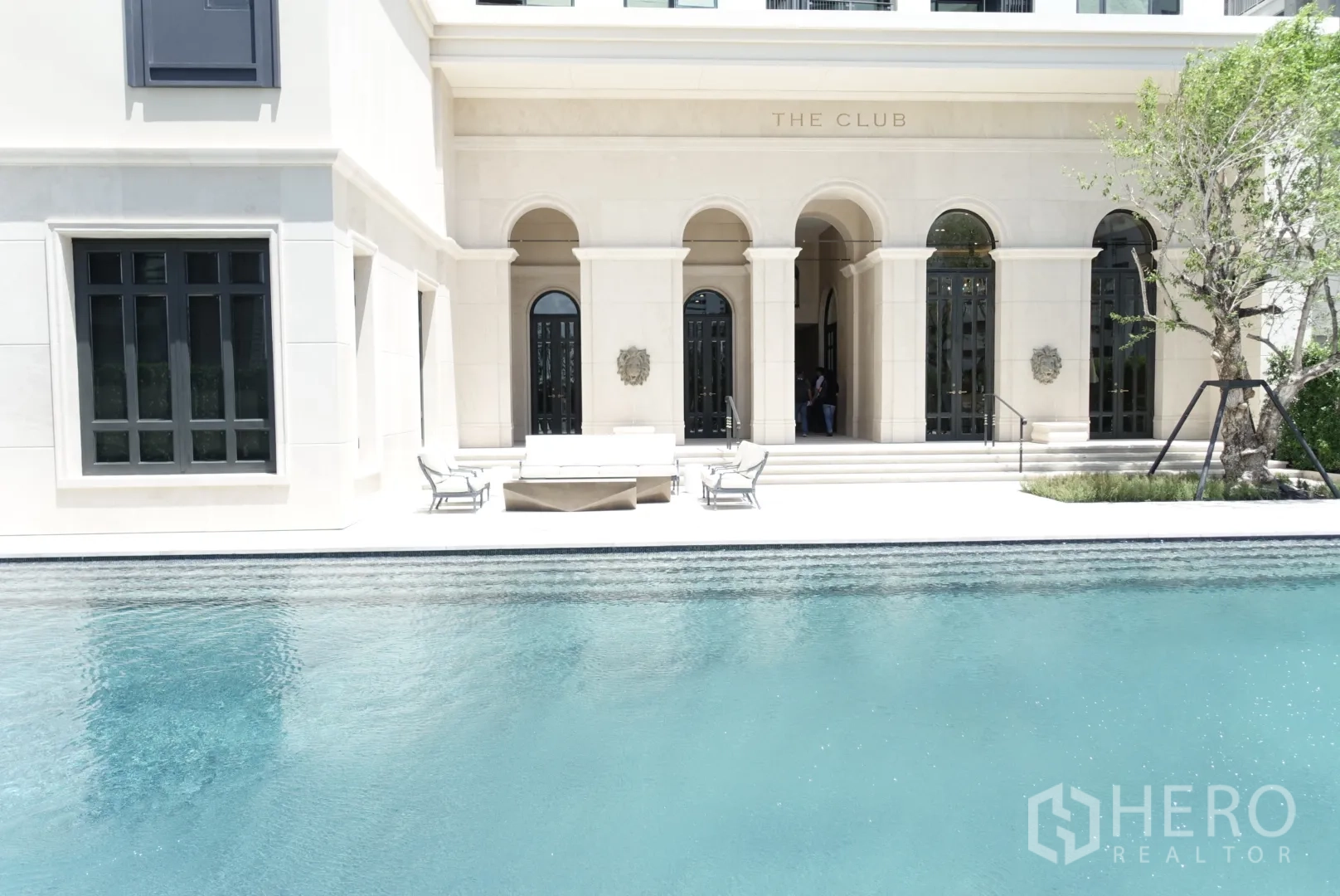 Condominium for rent or sale in Watthana, Bangkok - Outdoor swimming pool and seating at the condominium clubhouse with arched façade.