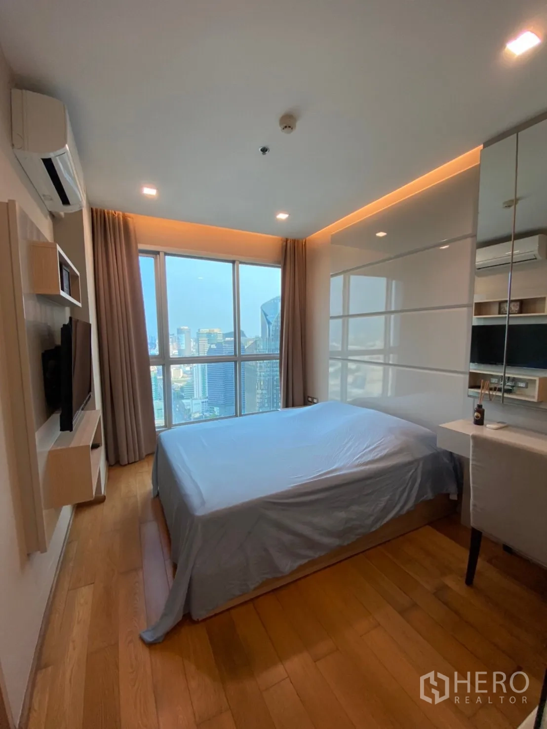 Condominium for rent in Ratchathewi, Bangkok - Bright bedroom with large window, soft cove lighting, built-in storage and expansive city view.