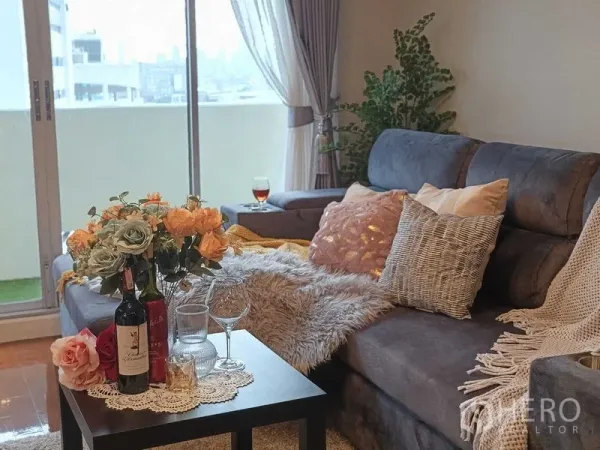 คอนโด ให้เช่าในKhlong Toei, Bangkok - ซอฟาสีเทาพร้อมหมอนอิง โต๊ะกาแฟจัดดอกไม้และไวน์ ใกล้ระเบียง