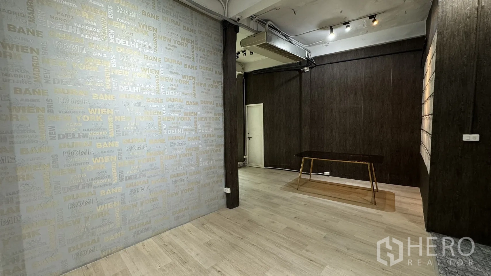 零售空间 出租在Watthana, Bangkok - 展厅一角，城市字样墙纸、射灯与现代桌子。
