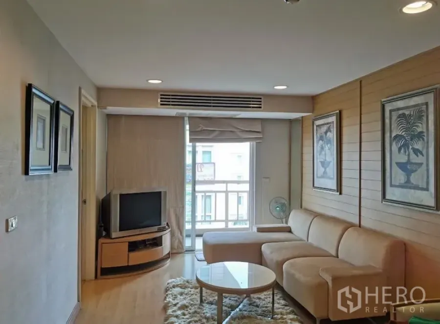 公寓 出售在Sathon, Bangkok - 采光良好的客厅，米色L型沙发、电视柜、墙面装饰画与通往阳台的推拉门