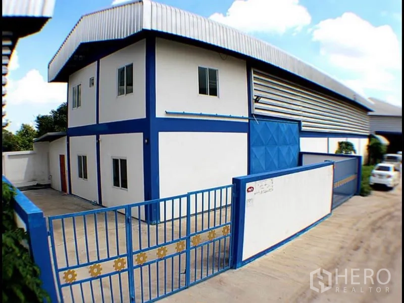 工厂 出租在Pak Kret, Nonthaburi - 两层办公楼与厂房一体的外观，带车道与金属栅栏大门