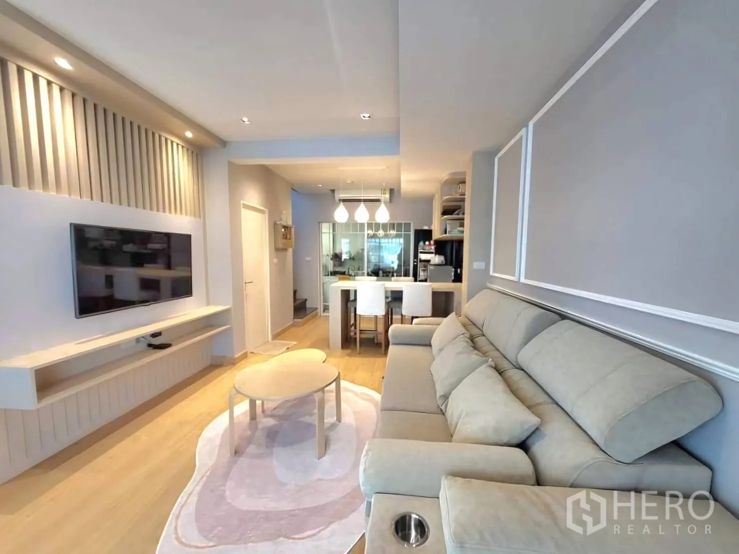 Townhouse for rent in Bang Phli, Samut Prakan - Bright living room with large sofa, built-in TV wall, recessed lighting and wood flooring.