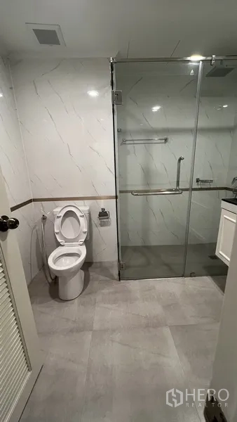Apartment for rent in Watthana, Bangkok - Modern bathroom with glass-enclosed shower, white marble-look walls and toilet.