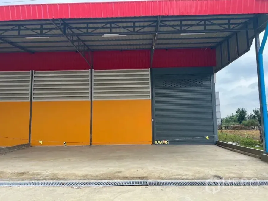 Warehouse for rent or sale in Sai Noi, Nonthaburi - Covered loading dock with a grey roller shutter, drainage channel, and colorful warehouse facade in Sai Noi.