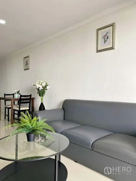 公寓 出租在Khlong Toei, Bangkok - 起居区细节：灰色沙发、玻璃茶几、餐桌与墙面装饰画。