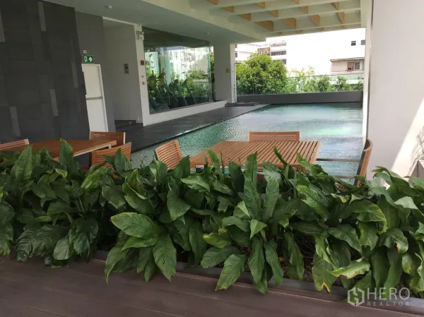 公寓 出售在Bang Rak, Bangkok - 有顶泳池平台，木质桌椅与绿植，可见健身房