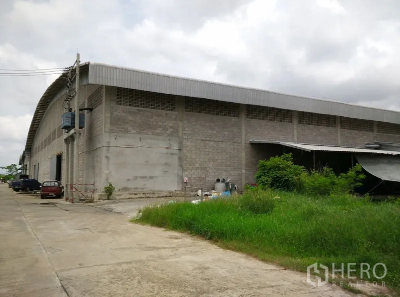 Factory for rent or sale in Krathum Baen, Samut Sakhon - Massive factory exterior in concrete block with ventilation blocks and a side yard for loading and storage.