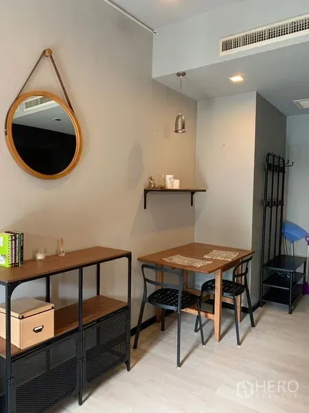 Condominium for sale in Watthana, Bangkok - Compact dining nook with wooden table for two, wall mirror, open shelf, and light wood floors.