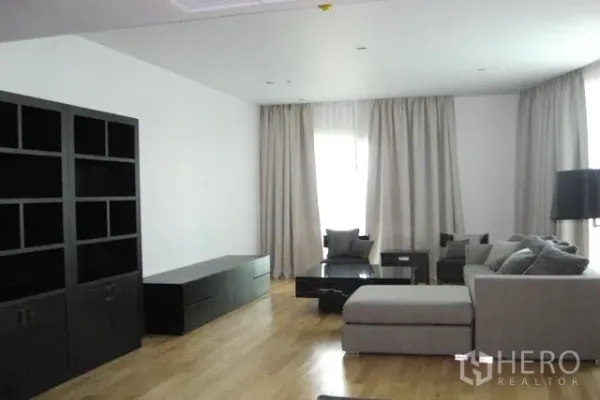 คอนโด ขายในKhlong Toei, Bangkok - ห้องนั่งเล่นกว้าง โซฟาแอลสีเทา ชั้นวางสีดำ พื้นไม้ และผ้าม่านสูง