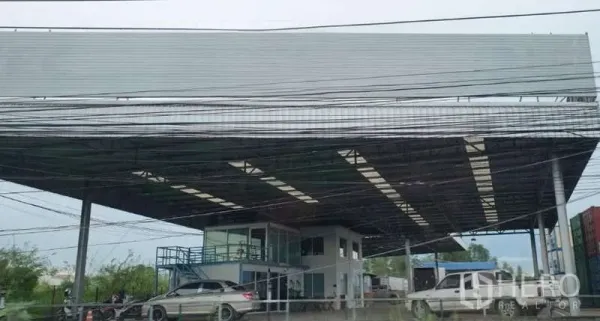 Land for sale in Si Racha, Chon Buri - Wide metal-roofed industrial yard with attached two-storey office and parking, seen from the roadside with overhead utility lines.