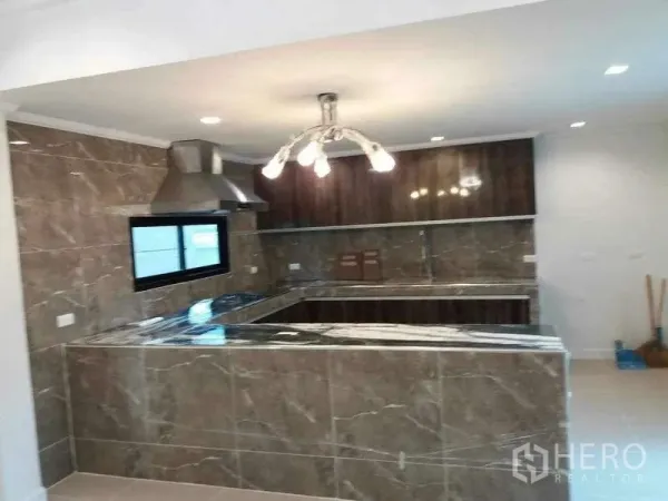 独立式住宅 出租或出售在Prawet, Bangkok - U形大理石纹厨房，配抽油烟机、吊柜与吊灯