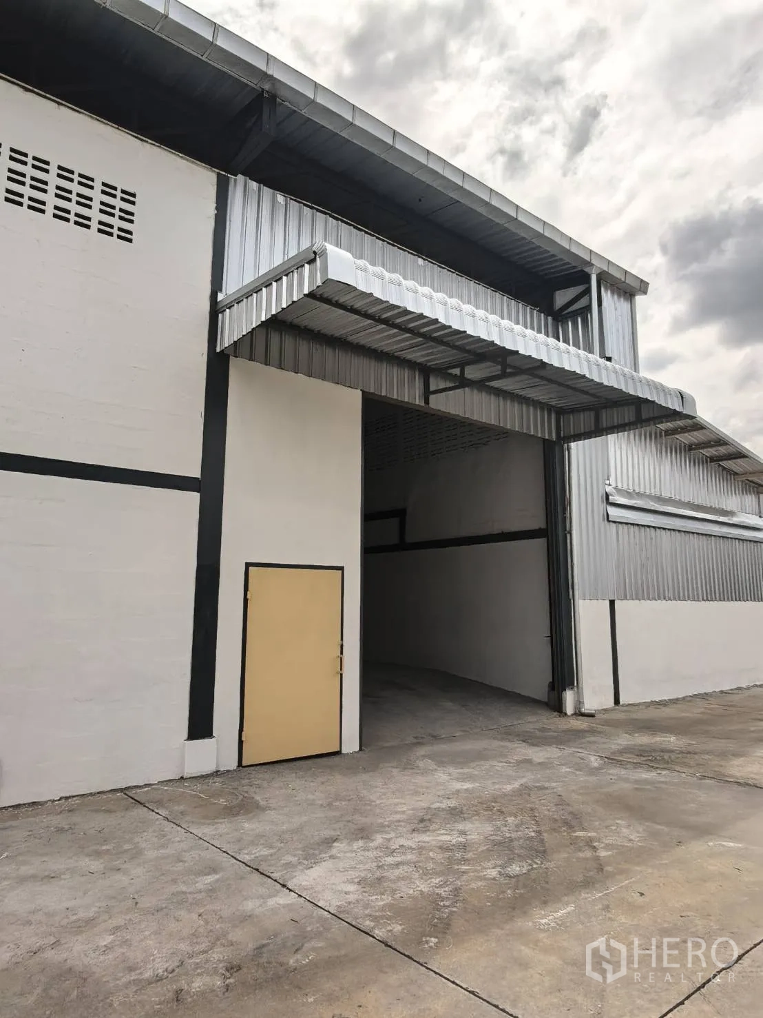 Warehouse for rent in Suan Luang, Bangkok - Warehouse exterior with metal cladding, covered loading canopy, and a tall entry bay over a concrete apron.