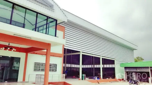 โรงงาน ขายในPathum Thani - ด้านหน้าโรงงานมีออฟฟิศกระจกมุมอาคารและช่องโหลดสินค้าภายใต้หลังคาเหล็ก
