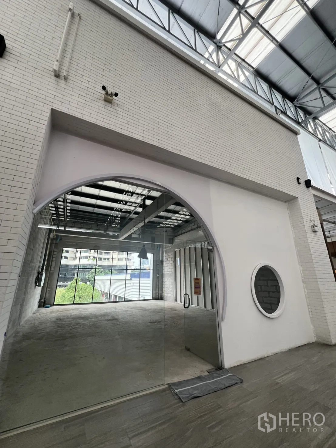 พื้นที่ขายปลีก ให้เช่า - มุมมองกว้างของหน้าร้านประตูกระจกโค้ง ใต้โถงหลังคาโปร่งแสง พร้อมทางเดินปูพื้น