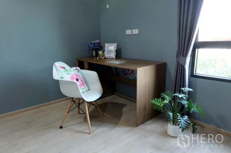 Townhouse for rent in Khlong Toei, Bangkok - Minimal study corner with wooden desk, white chair, potted plant and curtained window.