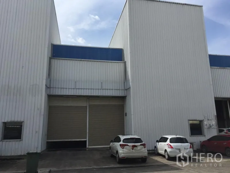 工厂 出租在Khlong Luang, Pathum Thani - 现代金属外墙厂房外观，配超大卷闸门，门前可停车。